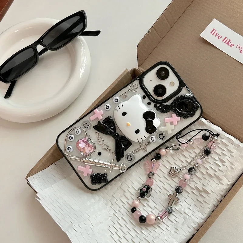 A Hello Kitty themed phone case with a black bow design, displayed alongside a box, sunglasses, and decorative beads.
