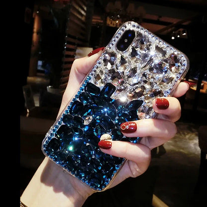 A person holding a black mobile phone with a clear rhinestone case filled with sparkling rhinestones.